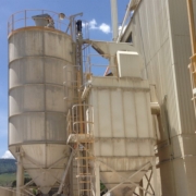 Outdoor industrial storage silo and baghouse dust collector system next to a processing facility. Outdoor industrial storage silo and baghouse dust collector system next to a processing facility.
